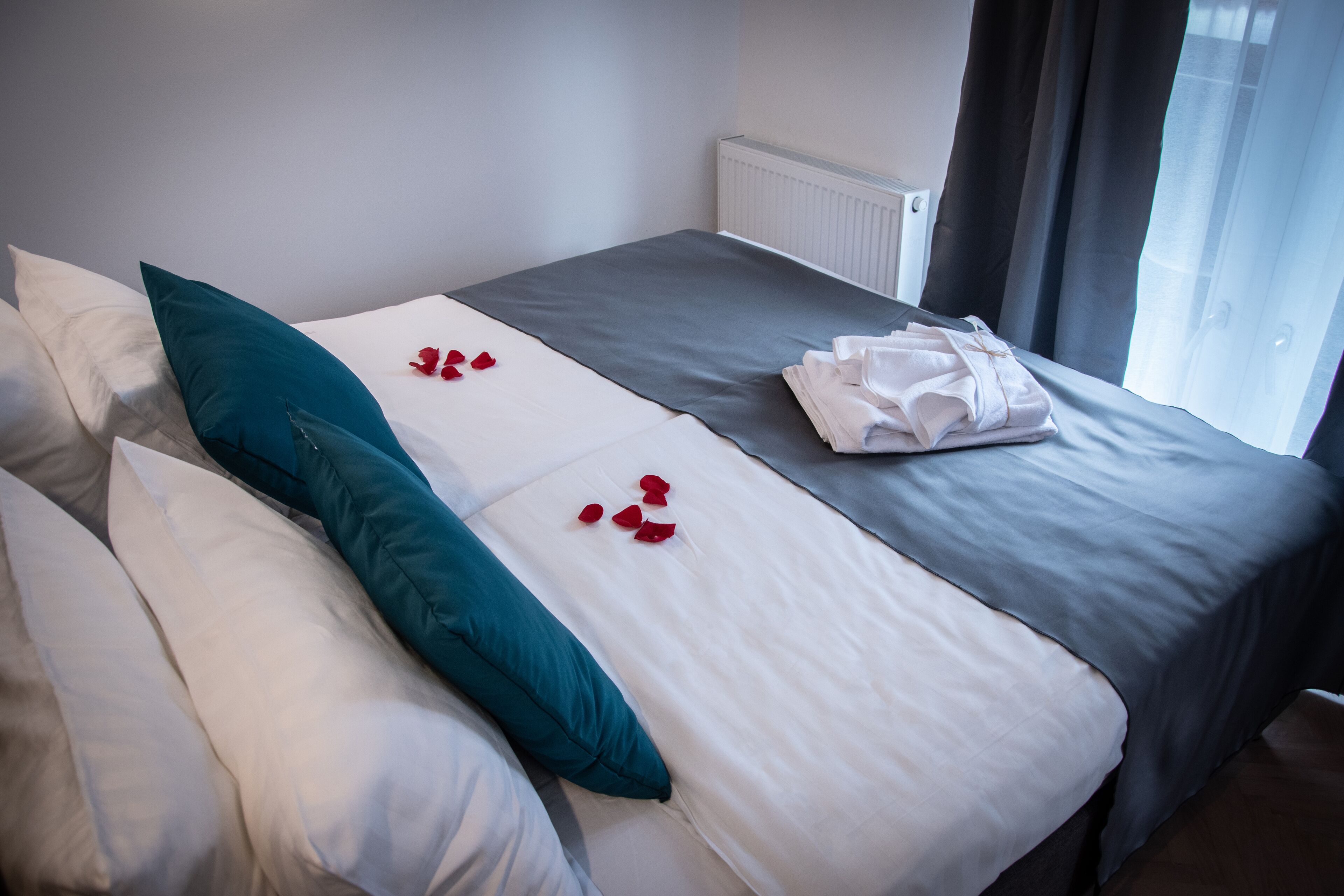 A hotel room with a neatly made bed, a set of towels, and a window with curtains.