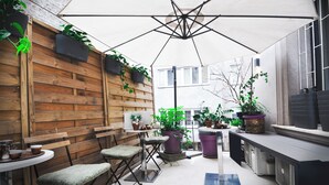 A cozy patio area with wooden benches, a table, and potted plants. - Hotel Petrakija (Sarajevo)
