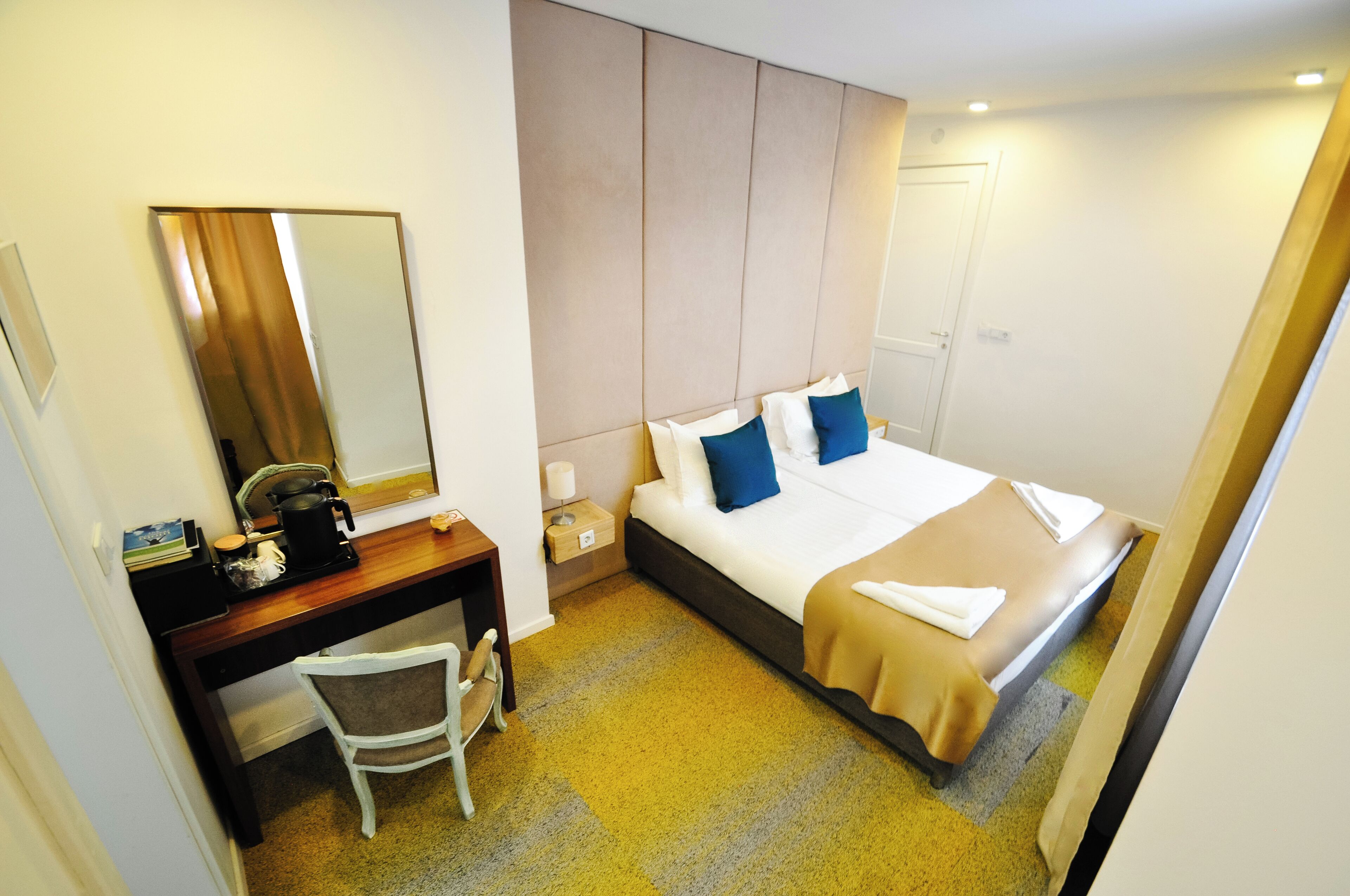 A hotel room with a bed, a desk, a chair, a mirror, and a door.