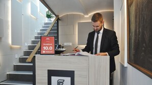 A man signing a document at a hotel reception desk with a staircase in the background. - Hotel Petrakija (Sarajevo)