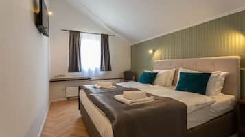A modern hotel room with a large bed, a flat-screen TV mounted on the wall, a window with curtains, and a radiator.