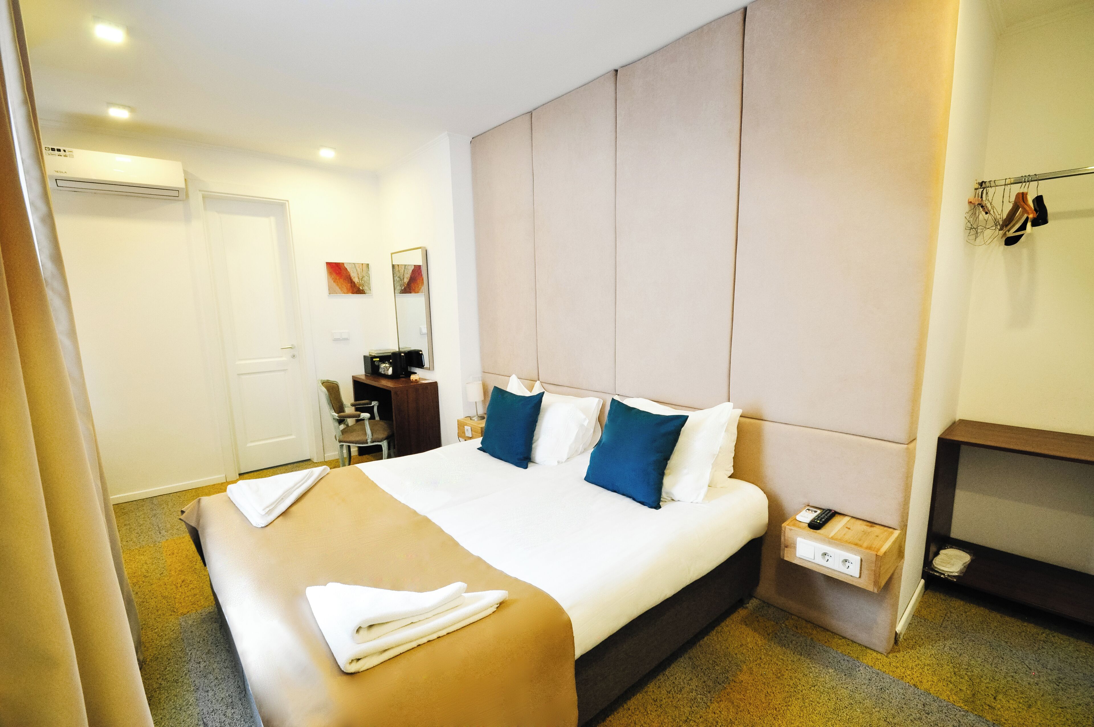 A hotel room with a large bed, a bedside table, a desk, and a wardrobe.