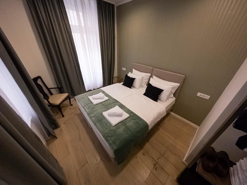 A hotel room with a bed, a chair, and a pair of shoes on a shelf.