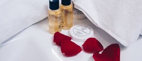 Two bottles of liquid soap and a bar of soap on a white surface with red rose petals.