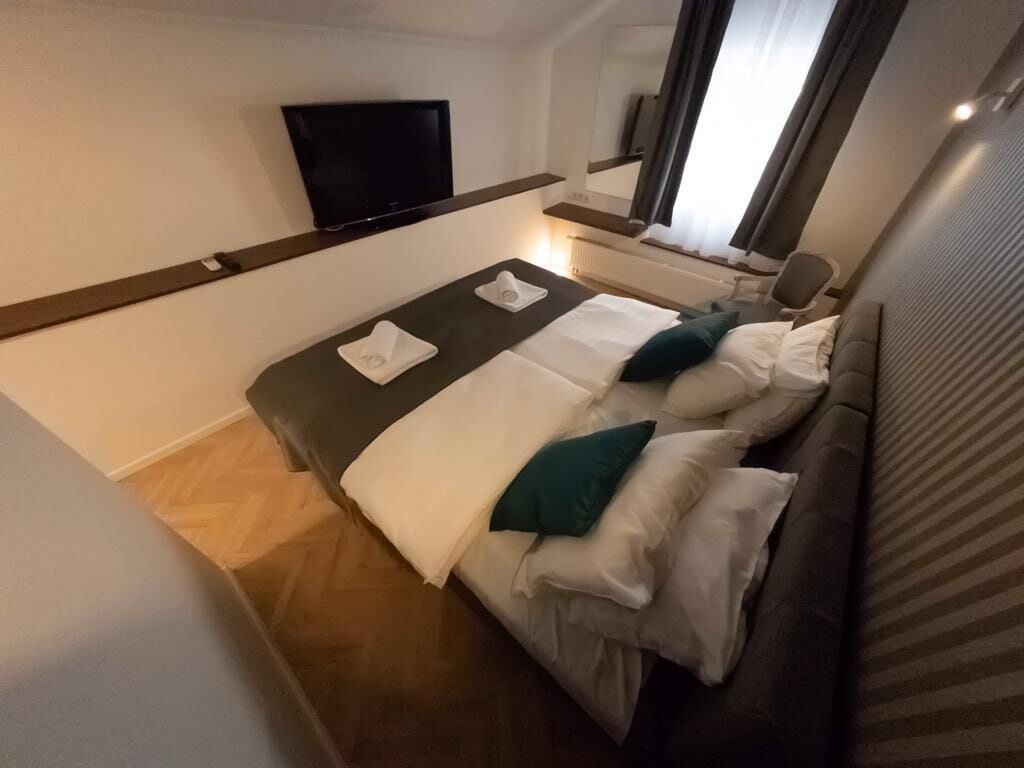 Une chambre d’hôtel compacte, dotée d’un lit simple, d’un téléviseur à écran plat fixé au mur et d’un grand miroir qui reflète la pièce.