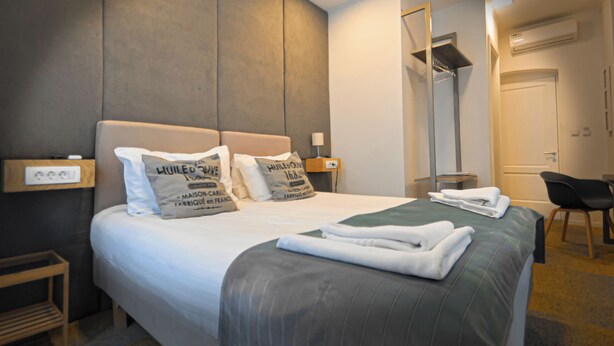 A hotel room with a large bed, two pillows, a bedside table with a lamp, a chair, and a wardrobe. - Hotel Petrakija (Sarajevo)