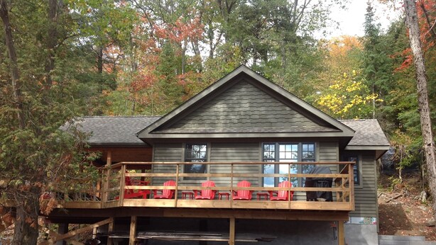 Una cabaña con terraza, sillas Adirondack rojas y un muro de contención de piedra.