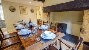 Un coin repas avec une table en bois dressée pour le repas, une cheminée et un mur en pierre.