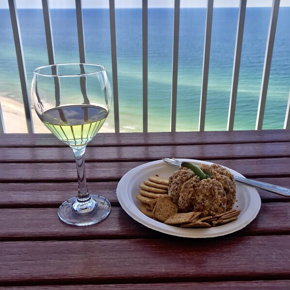A glass of white wine and a plate with food on a wooden table with a view of the ocean. - Great rates!! PENTHOUSE BEACHFRONT!  Most Stunning View of Gulf Shores!!   (Gulf Shores)