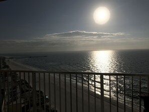Een strand met een pier die zich uitstrekt over de oceaan, bekeken vanaf een balkon met een hekwerk.