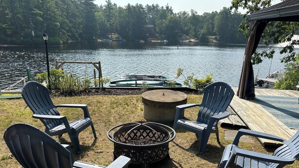 A lakeside deck with Adirondack chairs, a fire pit, and a view of the lake. - Cozy Lakefront Cottage (Winchendon)