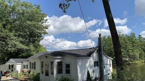 A single-story house with a chimney, surrounded by a garden and a lake. - Cozy Lakefront Cottage (Winchendon)