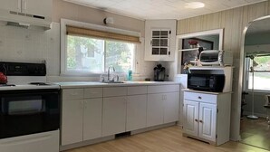 A kitchen with white cabinets, a microwave, and a stove. - Cozy Lakefront Cottage (Winchendon)