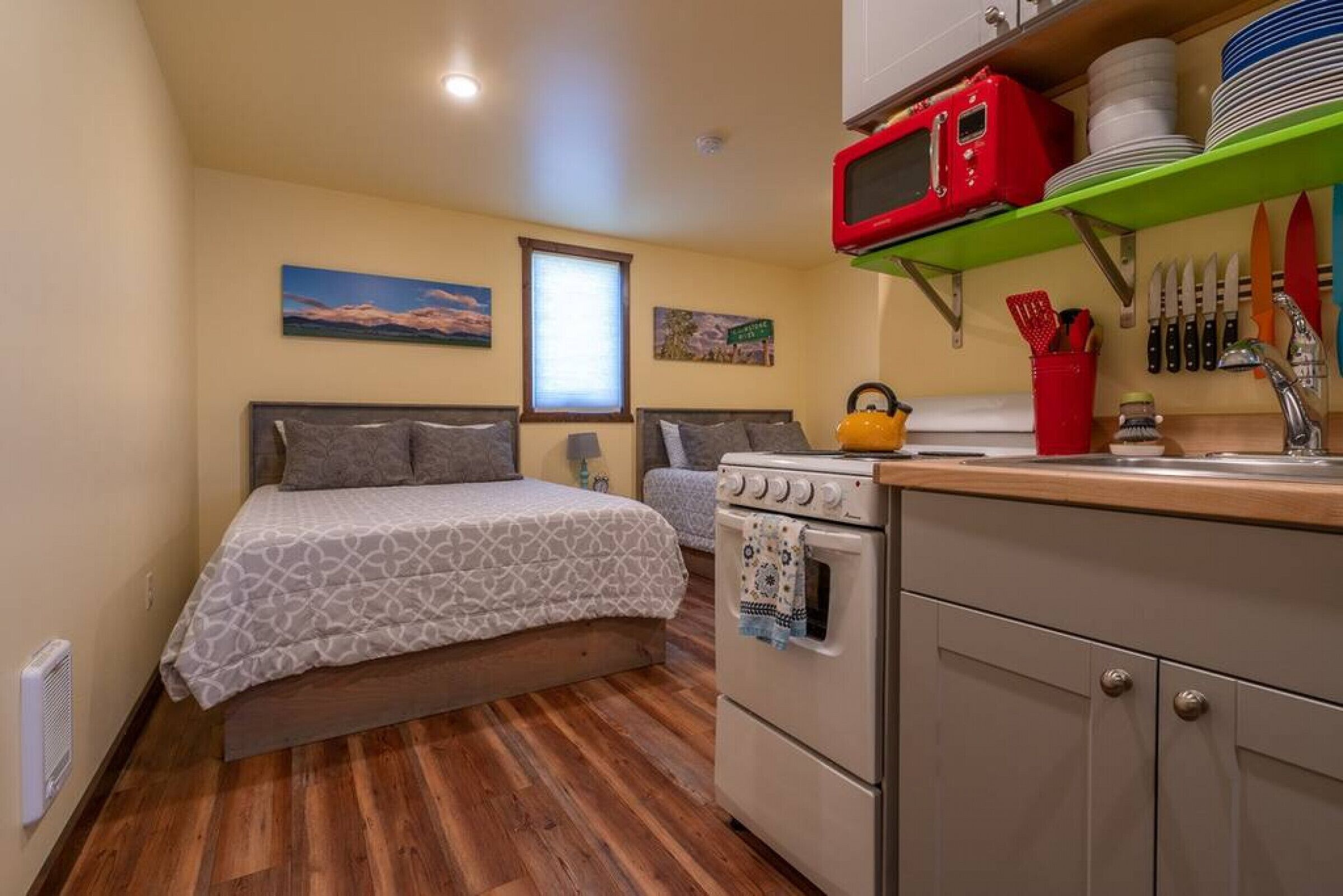 A compact room with a bed, kitchenette, and wooden flooring.