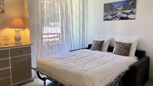 Ein Schlafzimmer mit einem Bett, einem Nachttisch mit Lampe, einem Fenster mit transparenten Vorhängen und einem Wandbild.