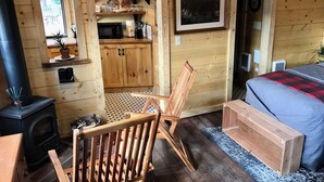 A cozy cabin room with a bed, a wooden chair, a small kitchen area with a microwave, and a fireplace.