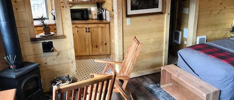 A cozy cabin room with a bed, a wooden chair, a small kitchen area with a microwave, and a fireplace.