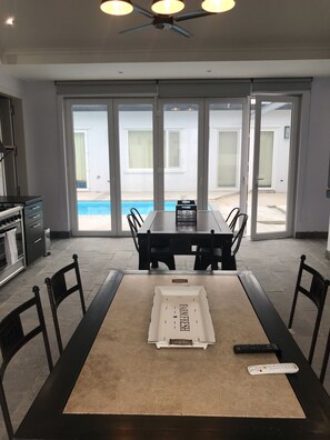 Uma área de refeições com mesa, cadeiras e vista para a piscina através de grandes portas deslizantes.
