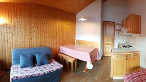 Ein gemütlicher Raum mit einem blauen Sofa, einem kleinen Tisch mit kariertem Tischlein und einer Küchenzeile mit Holzschränken und einem Herd.