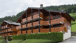 Ein mehrstöckiges Holzgebäude mit Balkonen, umgeben von Grünflächen und Hügeln.