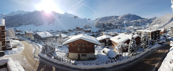 A snow-covered village with wooden buildings, a ski lift, and a mountain in the background.