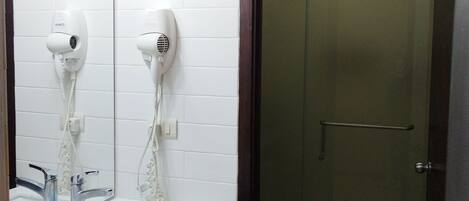 A bathroom with a mirror, two hair dryers, a sink, a toilet, and a glass-enclosed shower.
