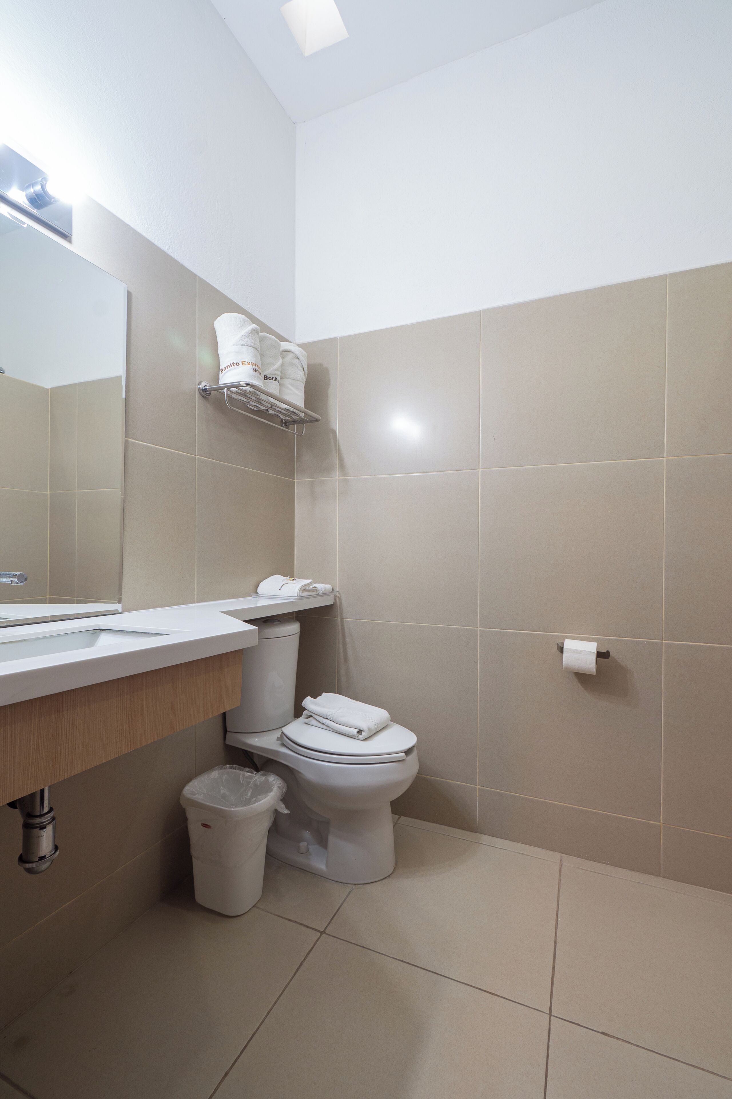Un baño con inodoro, lavamanos, espejo y cubo de basura.