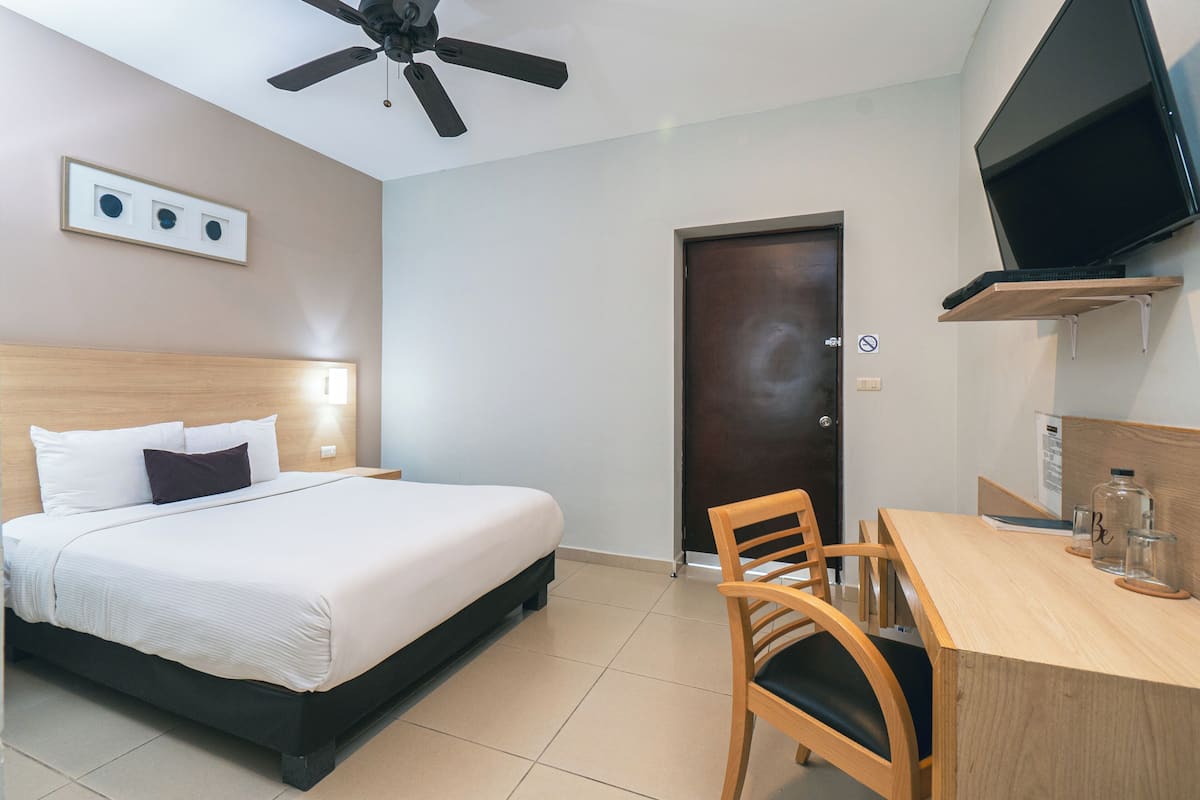 A hotel room with a bed, a desk, a chair, a television, and a ceiling fan.