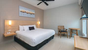 Ein Hotelzimmer mit einem Bett, Nachttischen, einem Deckenventilator, einem Gemälde, einem Sessel, einem kleinen Tisch und einem Fenster.