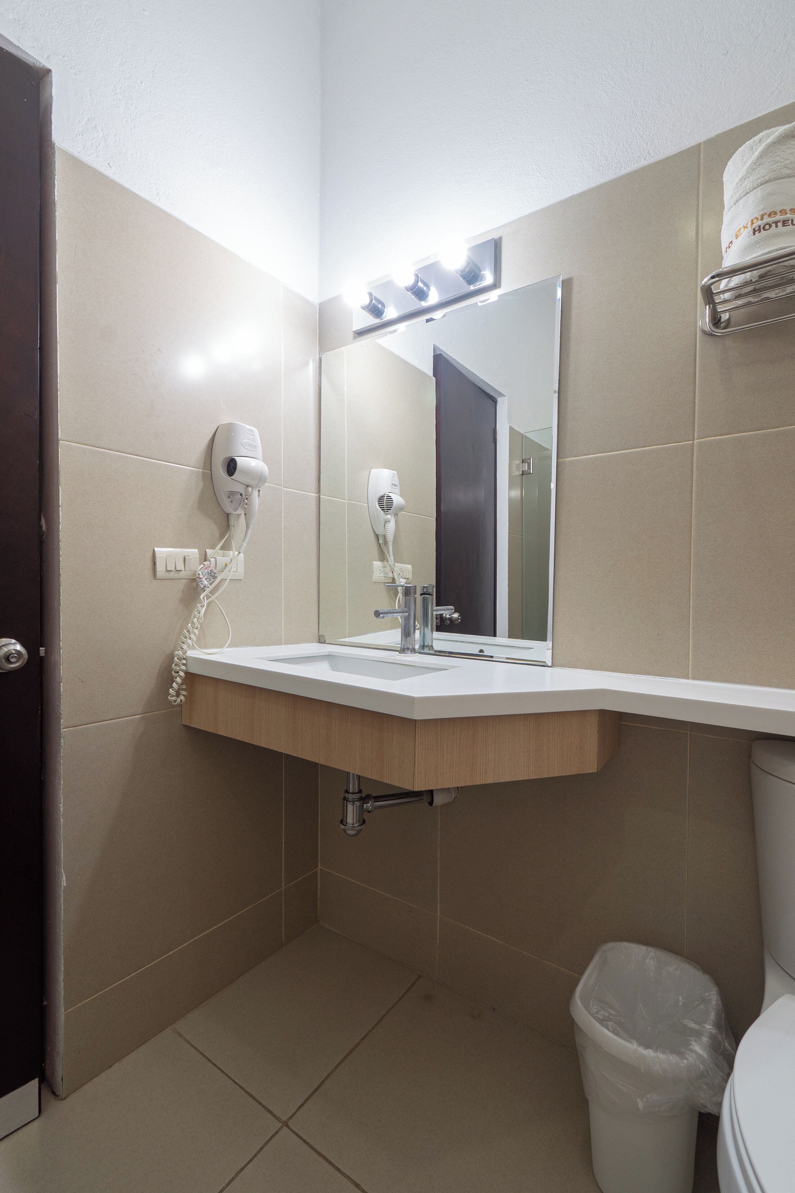 A bathroom with a sink, mirror, hairdryer, and a trash bin.