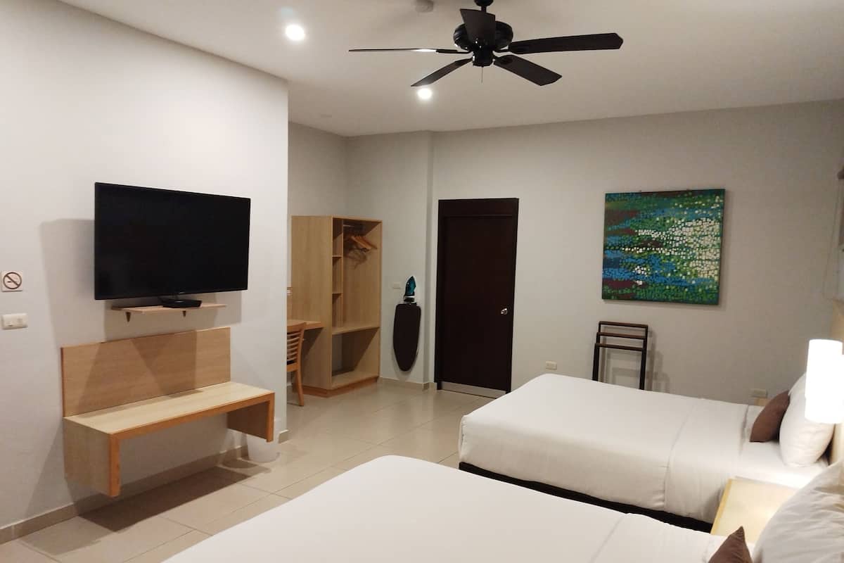 A hotel room with a bed, a TV, a ceiling fan, a wooden bench, a door, and a painting on the wall.