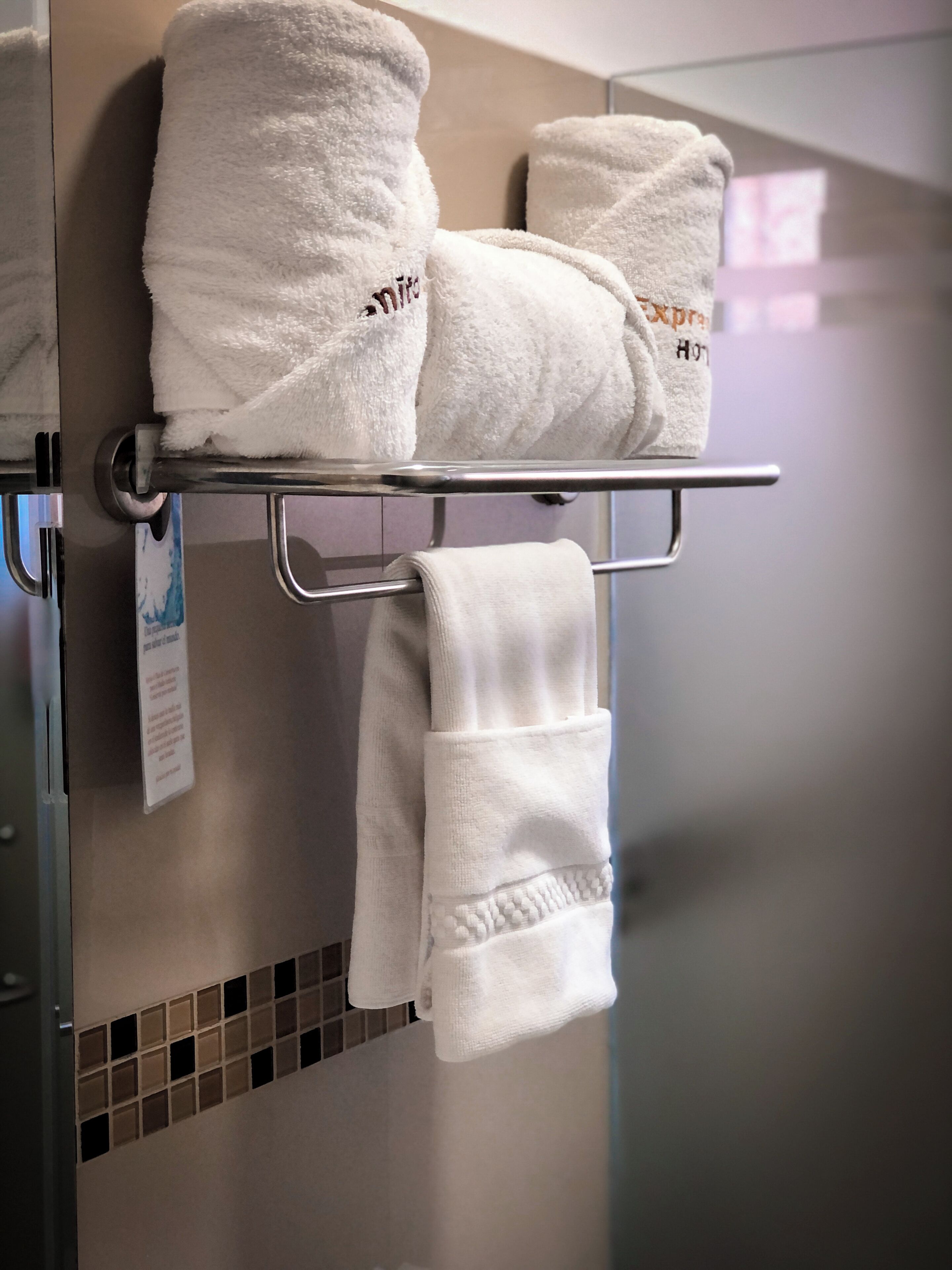 Ein Badezimmer mit Handtuchhalter, der drei weiße Handtücher und ein aufgehängtes Handtuch trägt.