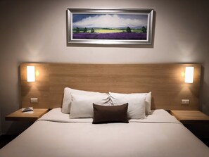 A hotel room with a wooden headboard, white bedding, a brown pillow, and a framed landscape painting above the bed. - Biza Express (Ciudad Valles)