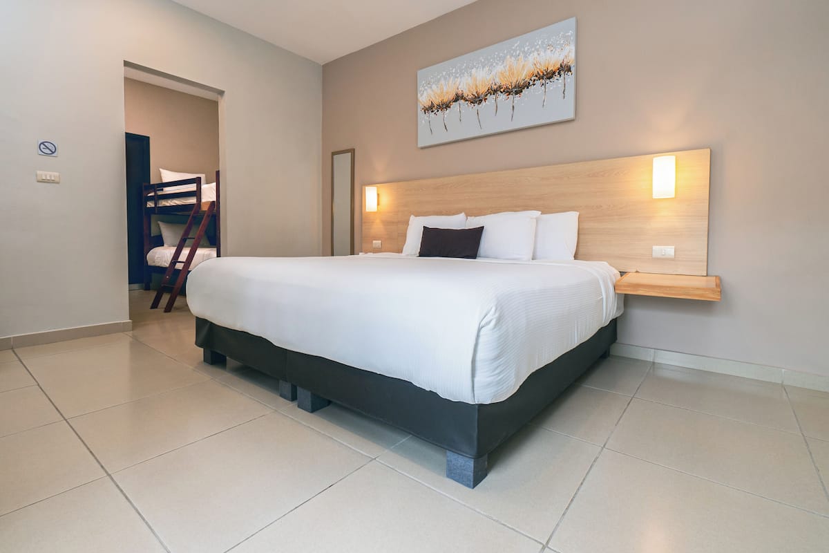 A modern hotel room with a large bed, a wooden headboard, a wall-mounted light, and a door leading to a balcony.