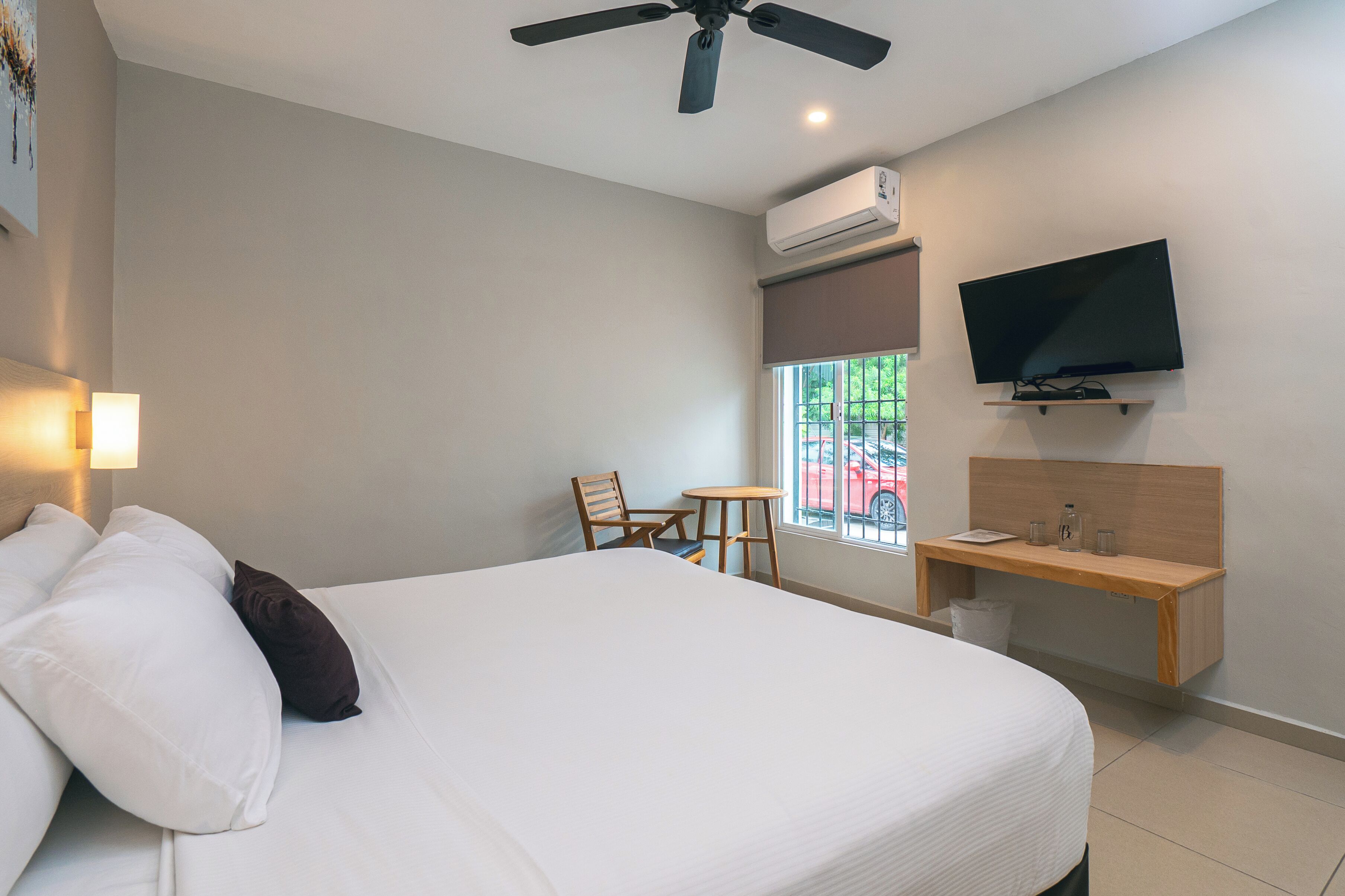 A hotel room with a bed, a desk, a chair, a television, and an air conditioning unit.