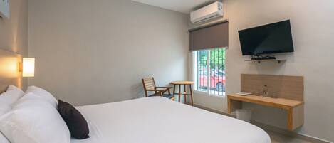 A hotel room with a bed, a desk, a chair, a television, and an air conditioning unit.