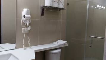 Een badkamer met toilet, wastafel, haardroger en een douchecabine van glas.