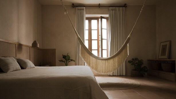 A bedroom with a hammock, a bed, a nightstand, a lamp, and a window with curtains. - Casa Montore by Barrio Mexico (Guadalajara)