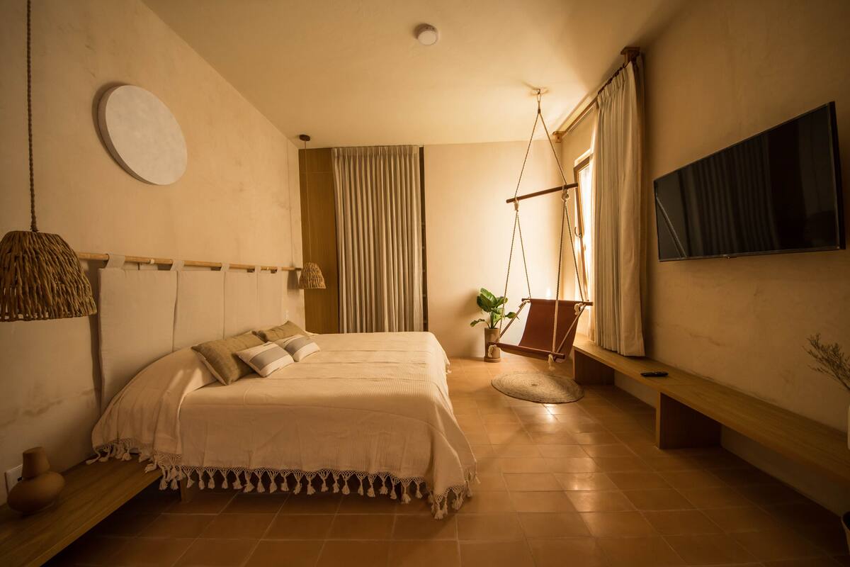 Ein Schlafzimmer mit einem großen Bett, einem Hängekorbstuhl, einem Fernseher und einem Topfpflanzen.