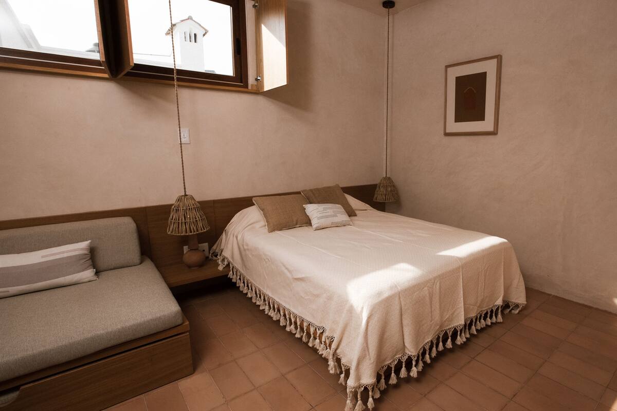 Ein Schlafzimmer mit einem Bett, einem Schlafsofa, einer Hängelampe und einem Bild an der Wand.
