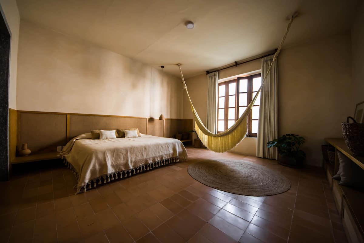 Ein Schlafzimmer mit einem Bett, einer Hängematte, einem runden Teppich und einem Fenster mit Vorhängen.