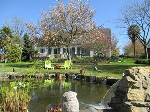 A garden with a pond, chairs, and a house with a porch.