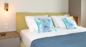 A neatly made bed with floral pillows, a wooden nightstand with a bowl, and a wall-mounted light fixture.