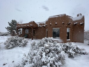 Een rustiek adobe huis met een besneeuwde buitenkant, een houten veranda en een raam met decoratieve details.