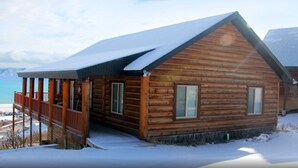 Une cabane en rondins dotée d’un balcon, d’un toit enneigé et offrant une vue sur une étendue d’eau.