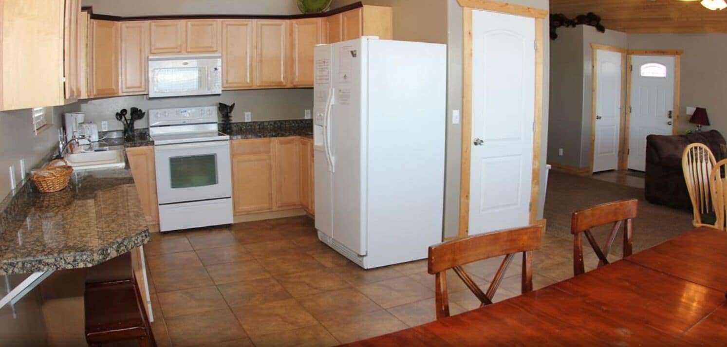 Una cocina con armarios de madera, un refrigerador blanco, una estufa y una encimera de granito.