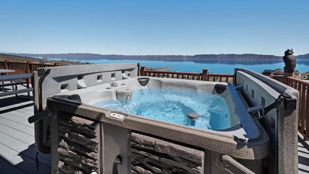 Un bain à remous sur une terrasse offrant une vue sur un lac et des montagnes.