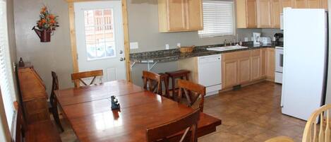 A kitchen with wooden cabinets, a white refrigerator, and a dining area with a wooden table and chairs.