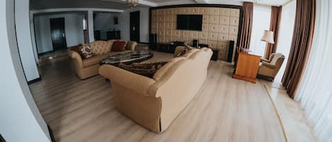 A spacious living room with a large sofa, a coffee table, and a television mounted on a padded wall.