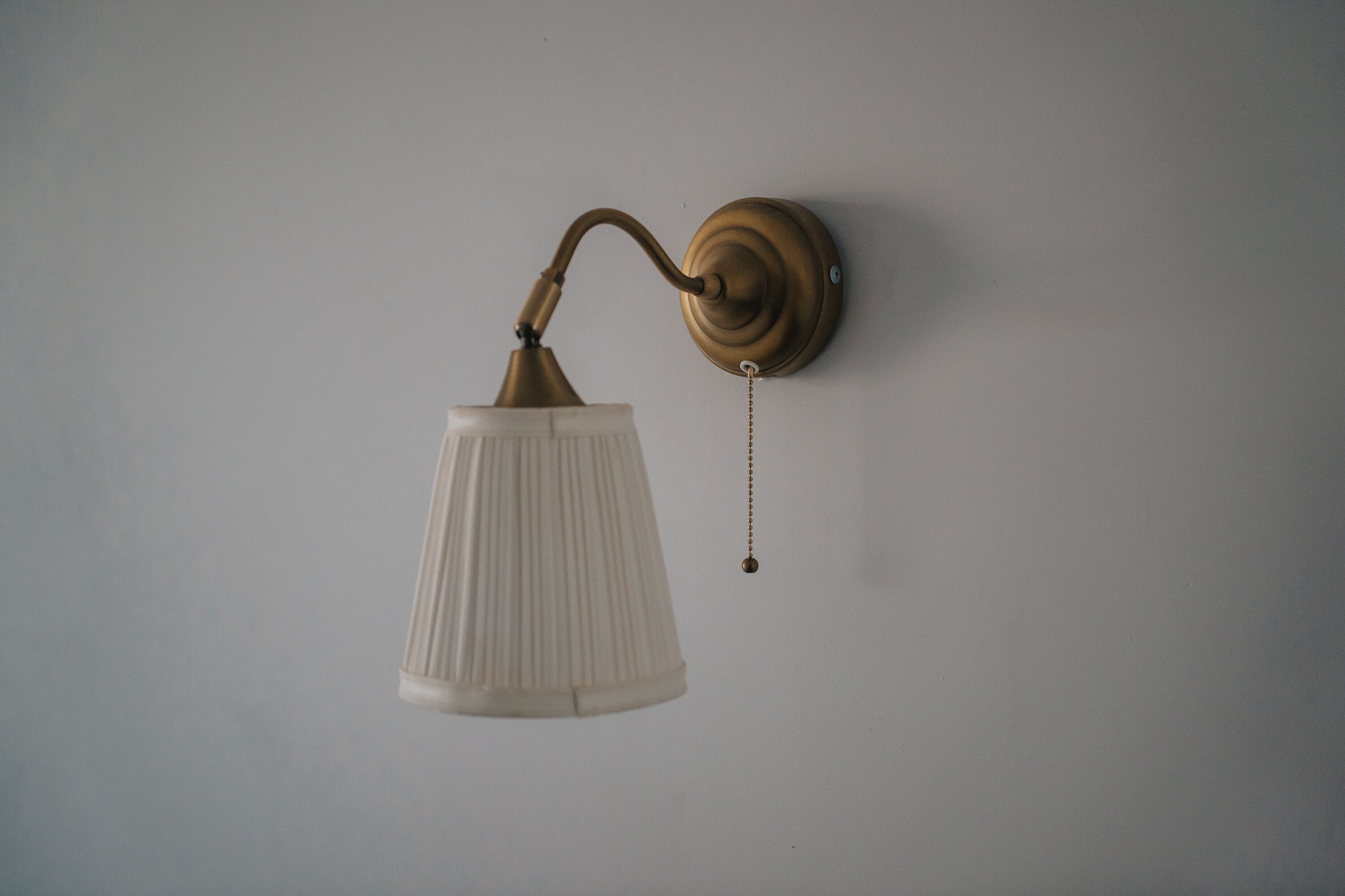 A wall-mounted light fixture with a white shade and a brass base.